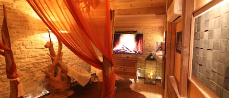 Une pièce chaleureuse avec un plancher en bois, un mur en pierre, une cheminée et un lit à baldaquin.