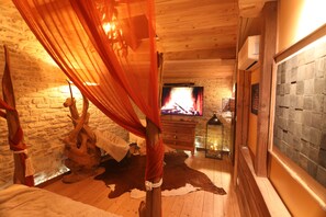Une pièce chaleureuse avec un plancher en bois, un mur en pierre, une cheminée et un lit à baldaquin.