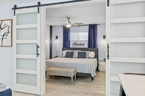 Une chambre à coucher comprenant un lit, un banc, un ventilateur de plafond et un luminaire fixé au mur.