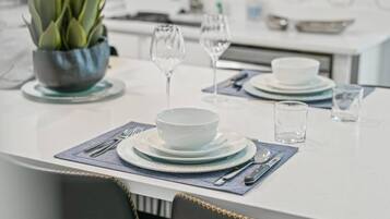 A modern dining area with a white table set for two, including plates, bowls, cutlery, and glasses.