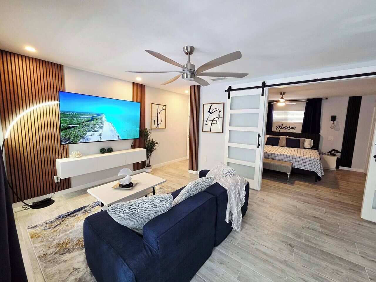 Ein modernes Wohnzimmer mit Flachbildfernseher, Deckenventilator, einer Couch und einem Bett mit Blick.