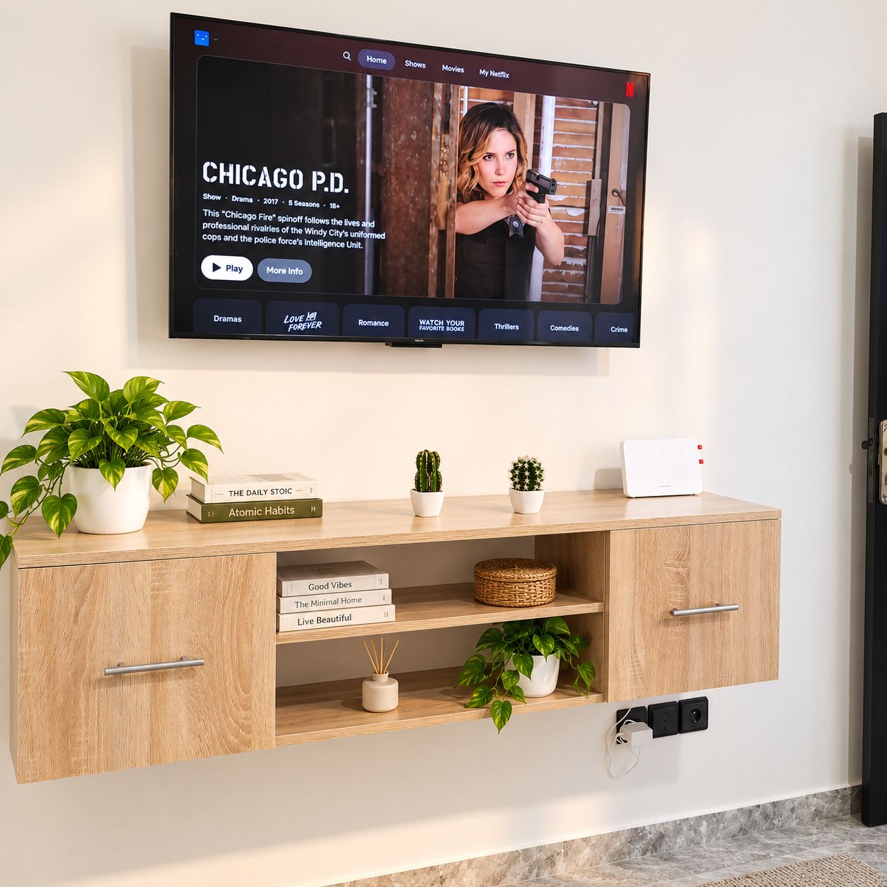 Un televisor de pantalla plana montado en la pared mostrando un programa titulado 'CHICAGO P.D.' con subtítulos. Debajo del televisor, hay un mueble de madera con libros, una planta en maceta y un pequeño dispositivo blanco.