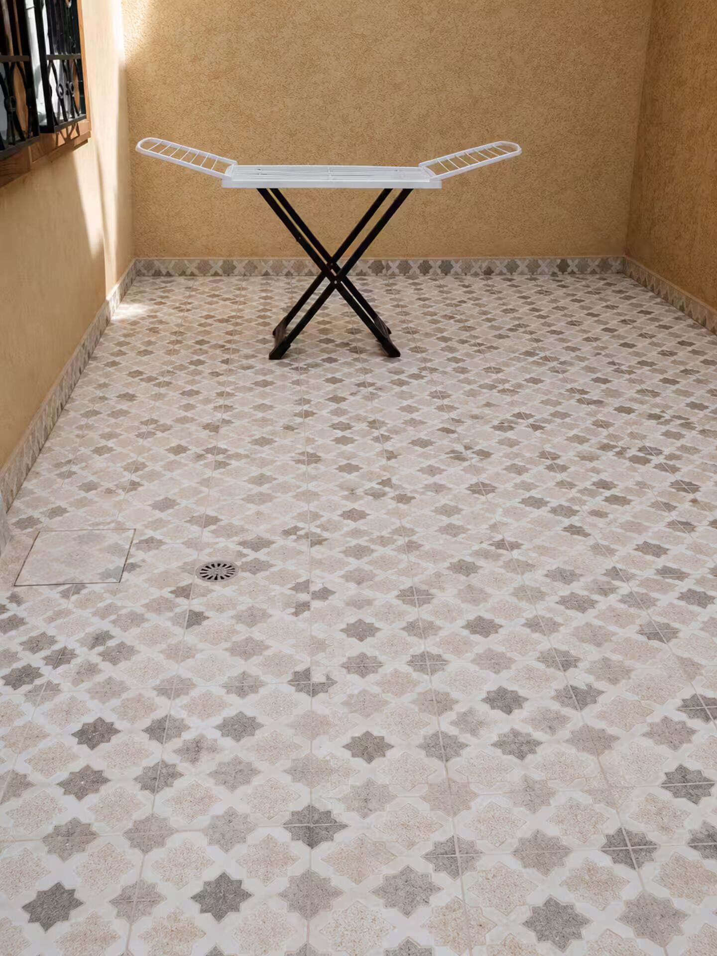 A room with a tiled floor, a white ironing board, and a window with metal bars.