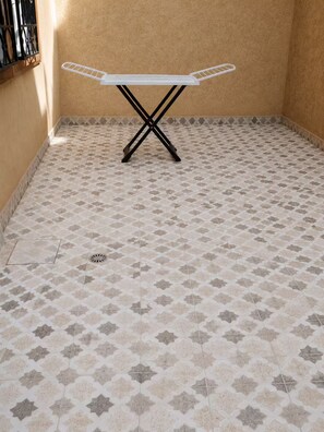A room with a tiled floor, a white ironing board, and a window with metal bars.