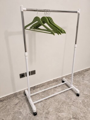 A white metal hanger rack with four green hangers against a wall.