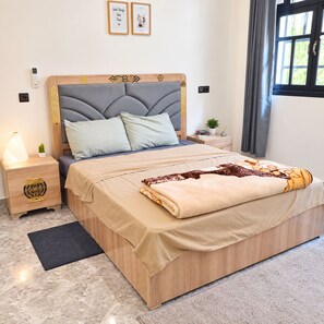 A bedroom with a bed, nightstands, a bedside lamp, a window with curtains, and a wall-mounted artwork.