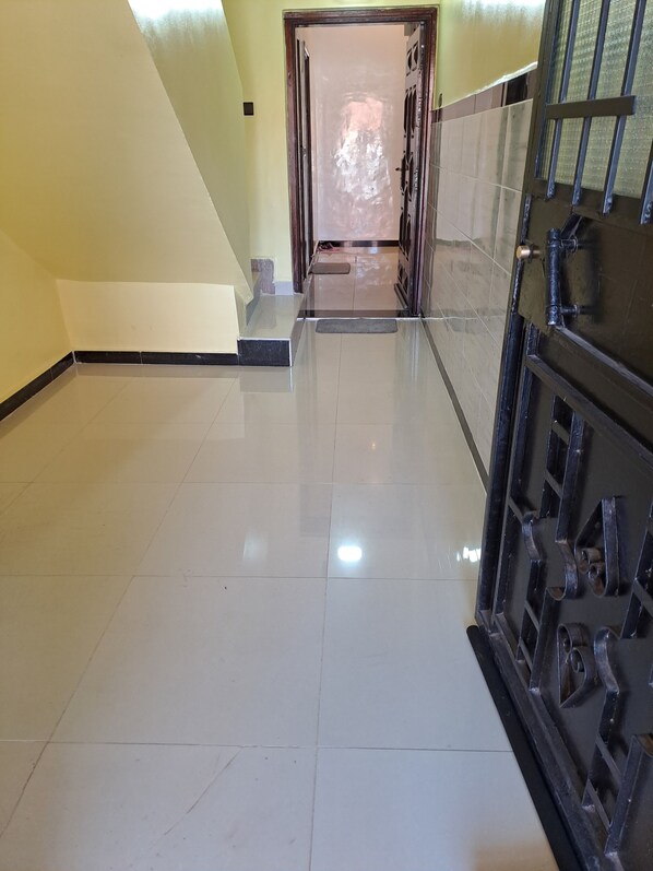 A hallway with a shiny tiled floor, a door at the end, and a metal gate on the right.