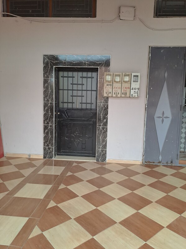 A room with a checkered floor, a black door with a metal grid, and a wall with numbered plaques.