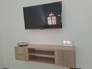 A flat-screen TV mounted on a wall above a wooden TV stand with a basket and a white device on it.