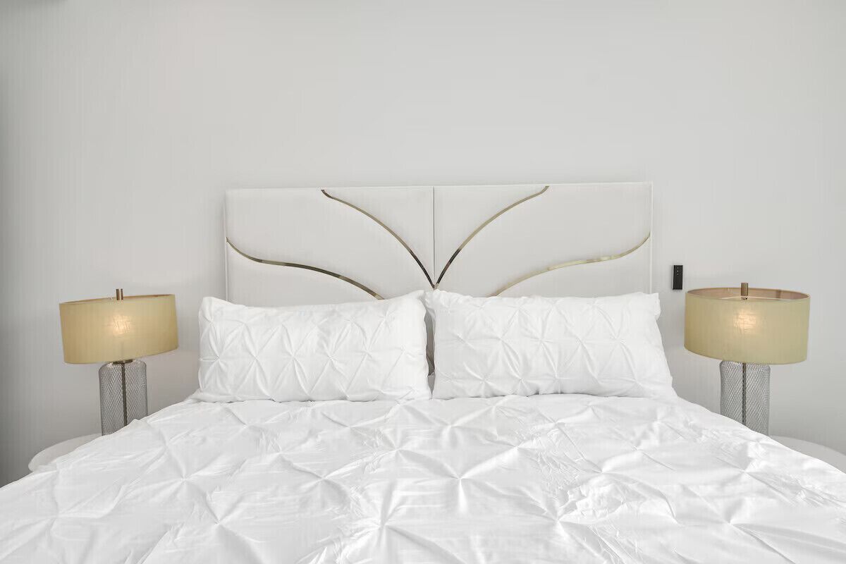 A bed with a white duvet and two pillows, flanked by two bedside lamps with beige shades.