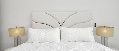 A bed with a white duvet and two pillows, flanked by two bedside lamps with beige shades.