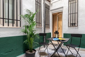 A small outdoor seating area with a table and chairs, a potted plant, and a door leading to a room. - Waou Essence I Salamanca - Short-Term (Madrid)
