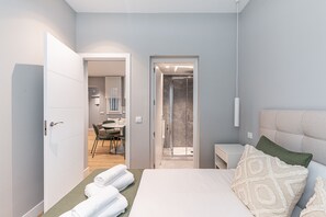 Ein modernes Schlafzimmer mit Bett, Nachttisch und Bad, das durch eine offene Tür sichtbar ist.