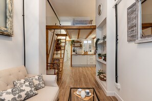 Ein kompakter Wohnraum mit einer Couch, einem Couchtisch mit Tassen, einer Wendeltreppe und einer Küchenzeile mit Schränken und einem Fenster.