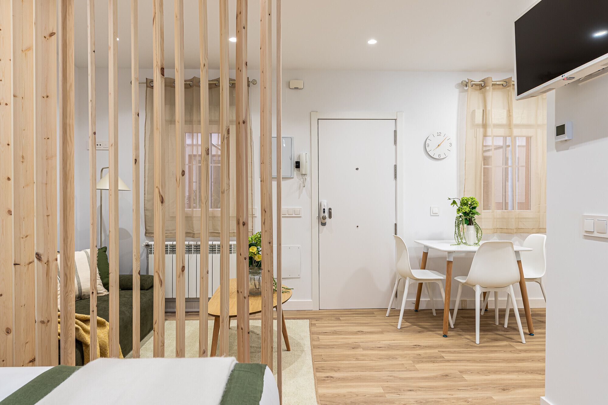 A room with a bed, a dining table with chairs, a TV mounted on the wall, and a door with a lock.