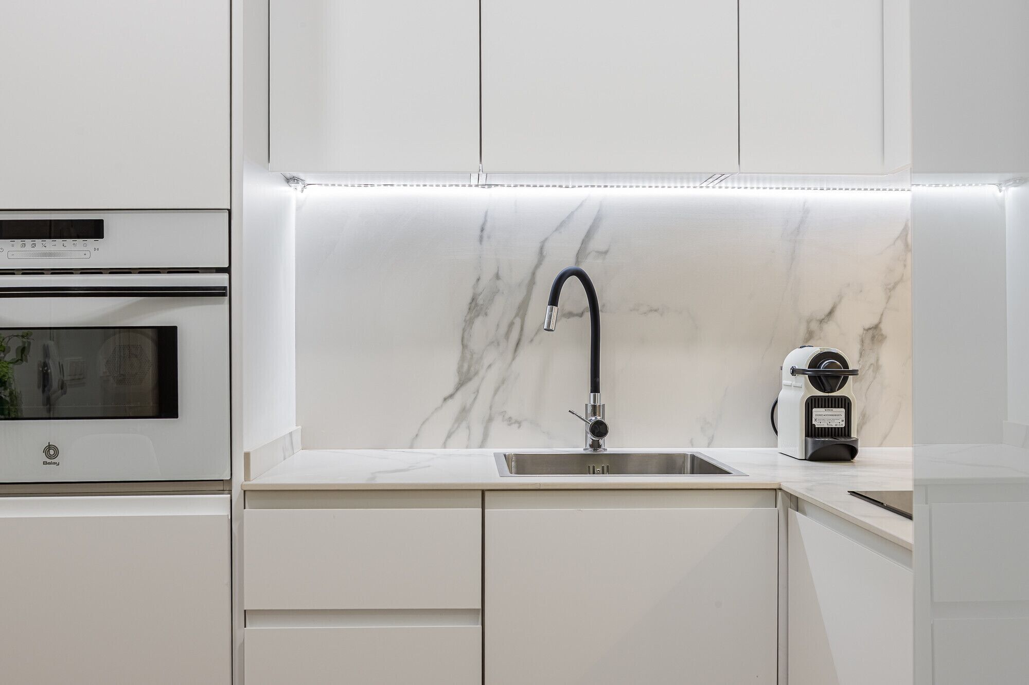 A modern kitchen with a built-in oven, a sink with a sleek faucet, and a coffee machine.