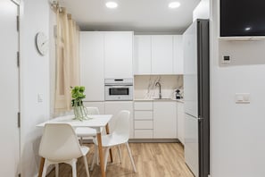 A compact kitchen with white cabinetry, a built-in oven, a microwave, a sink, and a black refrigerator. - Waou Cuatro Caminos II - Short-Term Rental (Madrid)