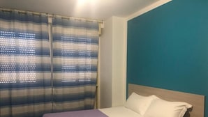 Een slaapkamer met een bed, gordijnen en een wand in blauwgroen.
