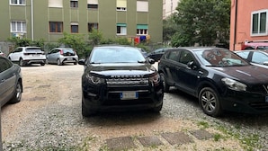 Een parkeerplaats met meerdere auto's, een gebouw met veel ramen en een boom.