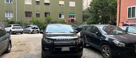 Un estacionamiento con varios automóviles, un edificio con múltiples ventanas y un árbol.