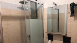 Een badkamer met een douchecabine van glas, een wastafel met spiegel erboven en een handdoekdispenser.