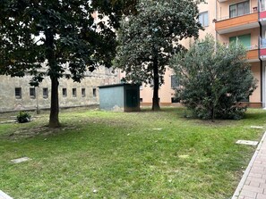 A courtyard with grass, trees, a small shed, and a building with windows and balconies. - Venicenight Apartment 25 (Venezia)