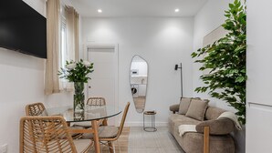 A compact living space with a dining area, a sofa, a mirror, and a potted plant. - Waou El Rastro II - Short-Term Rental (Madrid)