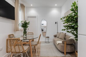 A compact living space with a dining area, a sofa, a mirror, and a potted plant. - Waou El Rastro II - Short-Term Rental (Madrid)