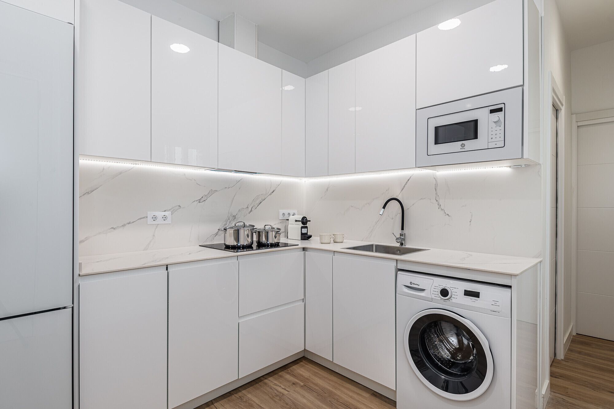 A compact kitchen with a built-in microwave, a sink, and a washing machine.