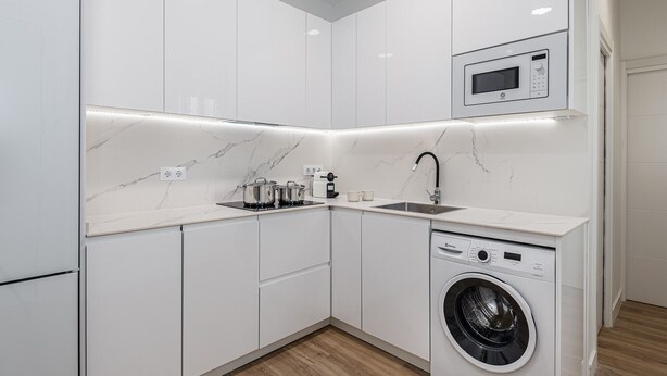 A compact kitchen with a built-in microwave, a sink, and a washing machine. - Waou El Rastro II - Short-Term Rental (Madrid)