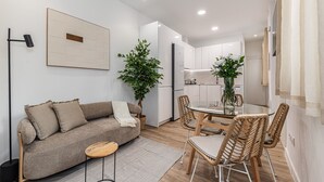 A modern living room with a sofa, a glass dining table, wicker chairs, and a potted plant. - Waou El Rastro II - Short-Term Rental (Madrid)