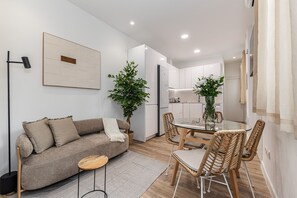 A modern living room with a sofa, a glass dining table, wicker chairs, and a potted plant. - Waou El Rastro II - Short-Term Rental (Madrid)