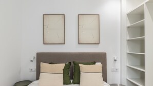 A bed with a headboard, two wall-mounted artworks, bedside lamps, and a small round table. - Waou El Rastro II - Short-Term Rental (Madrid)