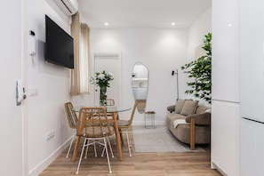 A modern living space with a dining area, a sofa, a TV mounted on the wall, and a potted plant. - Waou El Rastro II - Short-Term Rental (Madrid)