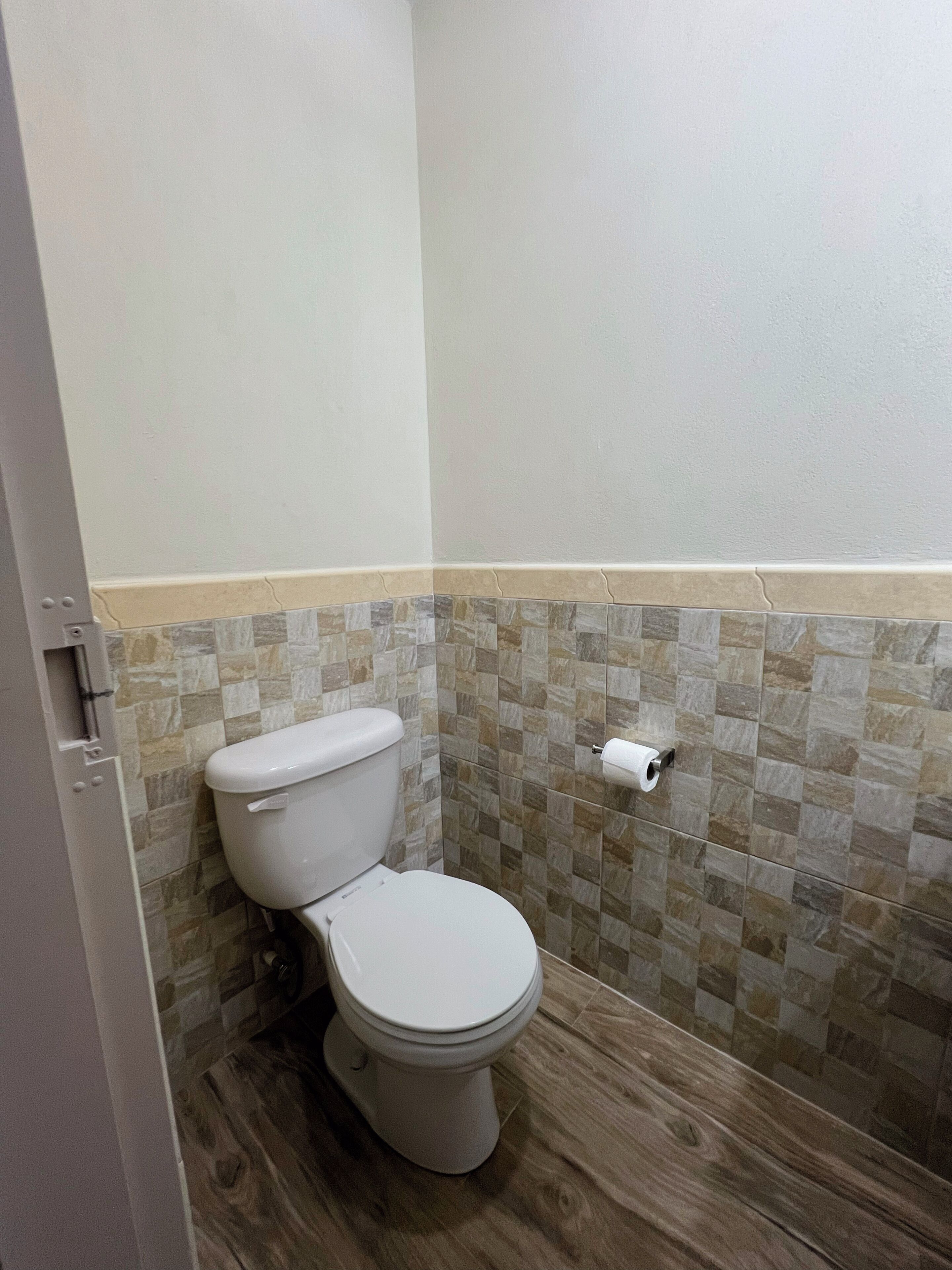 Une petite salle de bain avec des toilettes, un plancher en bois et un mur carrelé.