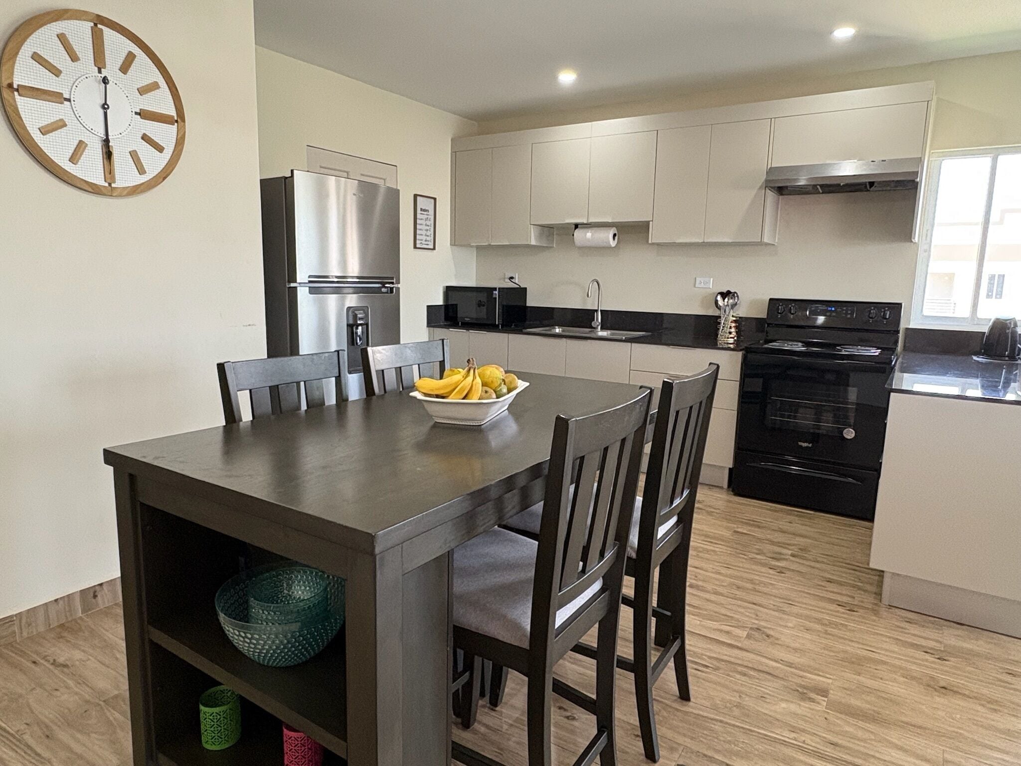 Une cuisine moderne avec une table à manger, des chaises, un réfrigérateur, une cuisinière, un four à micro-ondes et une horloge au mur.