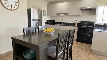 Une cuisine moderne avec une table à manger, des chaises, un réfrigérateur, une cuisinière, un four à micro-ondes et une horloge au mur.