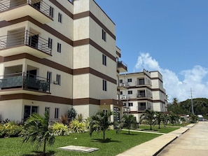 A multi-story residential building with balconies, a well-maintained lawn, and a clear sky.