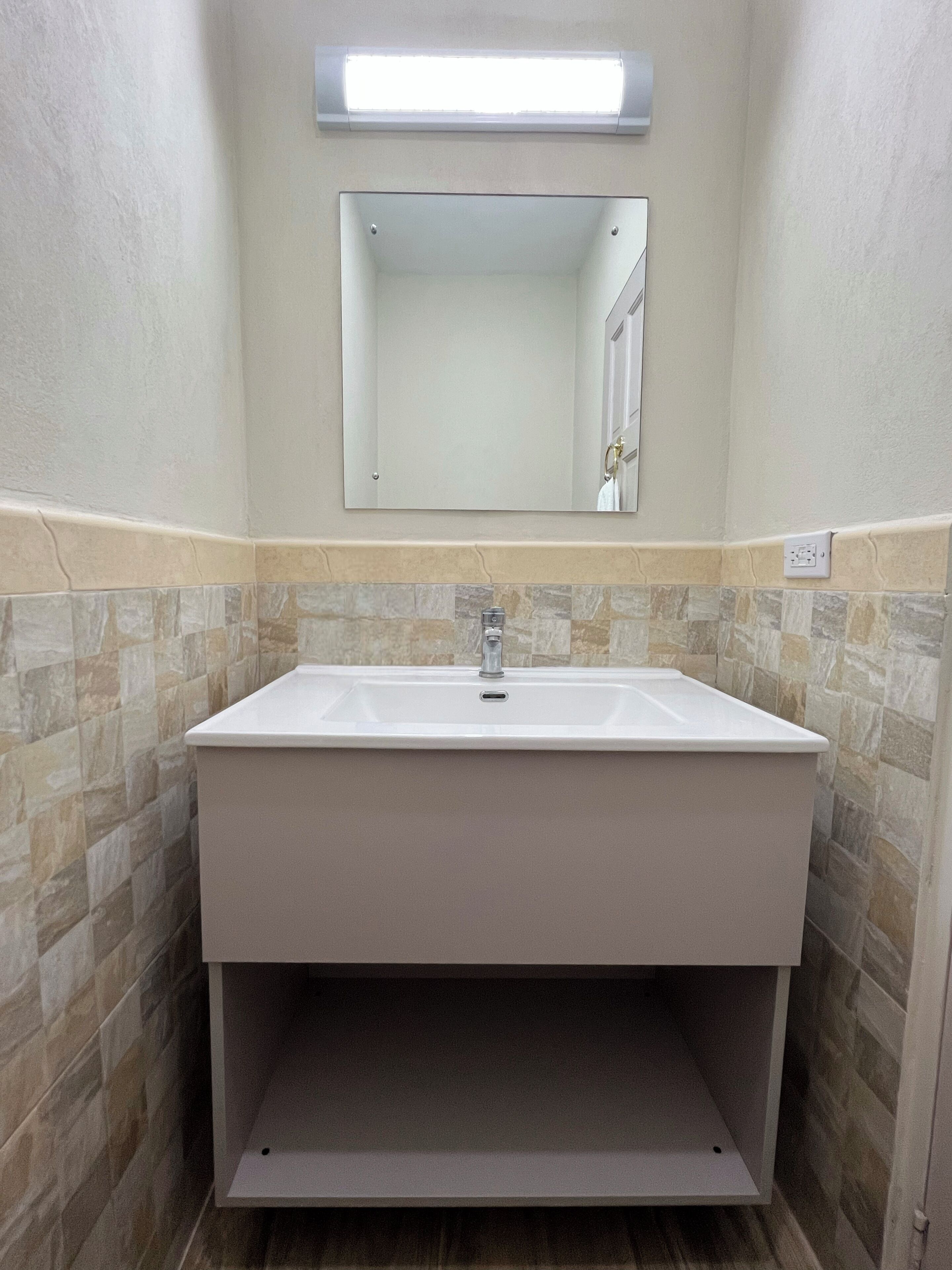Une salle de bain avec un lavabo rectangulaire, un miroir au-dessus et un luminaire fixé au mur.