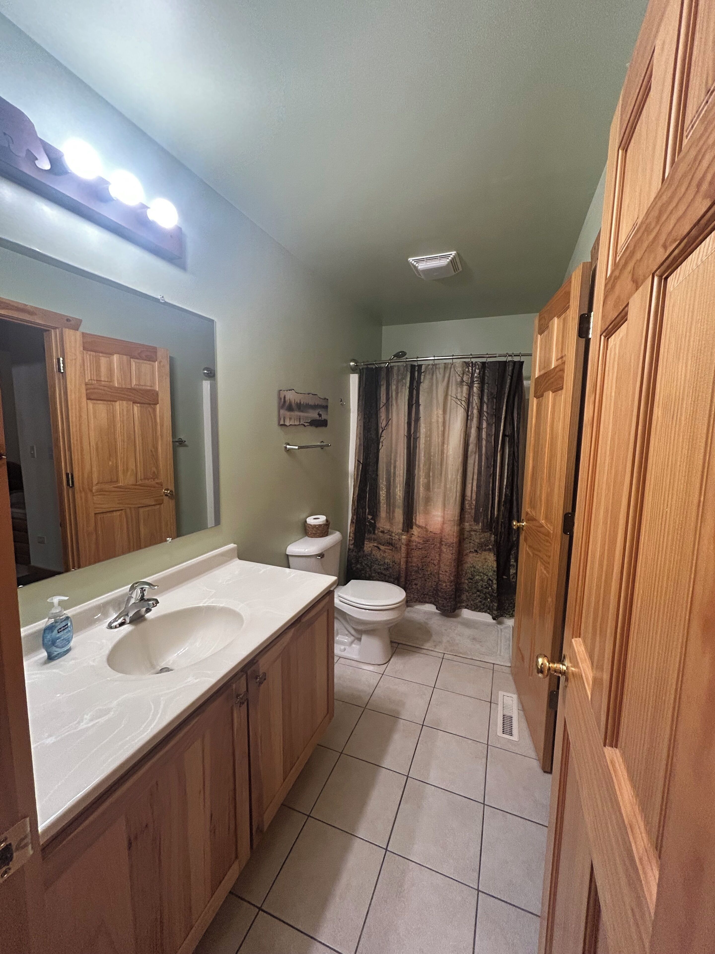 Une salle de bain avec un meuble-lavabo en bois, un lavabo blanc, des toilettes et un rideau de douche.