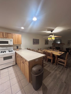 A kitchen with a central island, wooden cabinets, a microwave, stove, and a dining area with a table and chairs.
