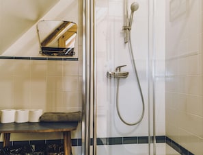 Une douche équipée d’un pommeau de douche à main et d’un robinet mural. Un miroir est placé au-dessus du lavabo, et une serviette est posée sur le comptoir.