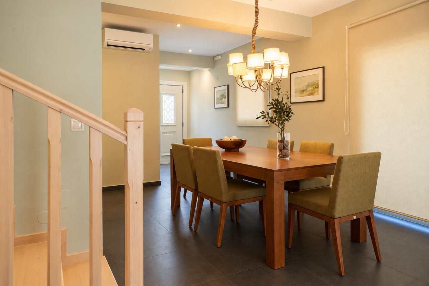 A dining area with a wooden table and chairs, a chandelier, and a vase with a plant.