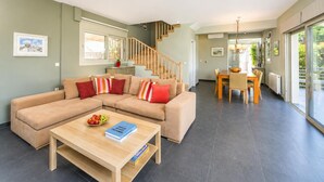 A modern living room with a sectional sofa, a dining table with chairs, and a staircase leading to an upper level. - Villa Oleana - Three Bedroom Villa, Sleeps 6 (Lefkada City)