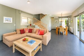 Ein modernes Wohnzimmer mit einer Eckcouch, einem Esstisch mit Stühlen und einer Treppe, die zu einer oberen Ebene führt.