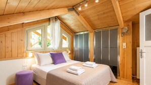 A wooden-paneled room with a bed, a small purple stool, and a door with a towel rack. - Villa Oleana - Three Bedroom Villa, Sleeps 6 (Lefkada City)