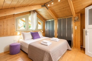 Ein Zimmer mit Holzwänden, einem Bett, einem kleinen violetten Hocker und einer Tür mit Handtuchhalter.