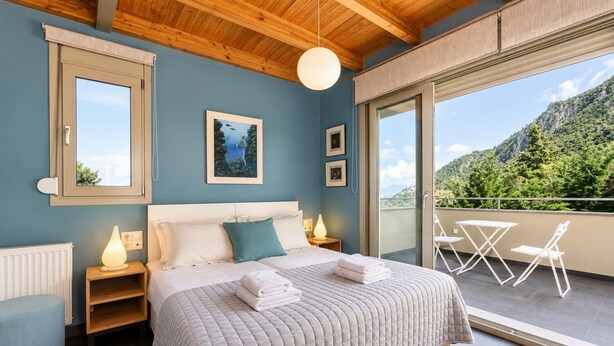 A bedroom with a large bed, bedside tables, a view of the outdoors, and a balcony with chairs. - Villa Oleana - Three Bedroom Villa, Sleeps 6 (Lefkada City)