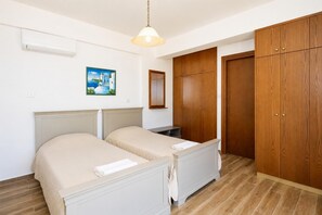 A bedroom with two beds, a wooden wardrobe, a painting on the wall, and an air conditioning unit. - Pomos View Villa - Four Bedroom Villa, Sleeps 8 (Pomos)