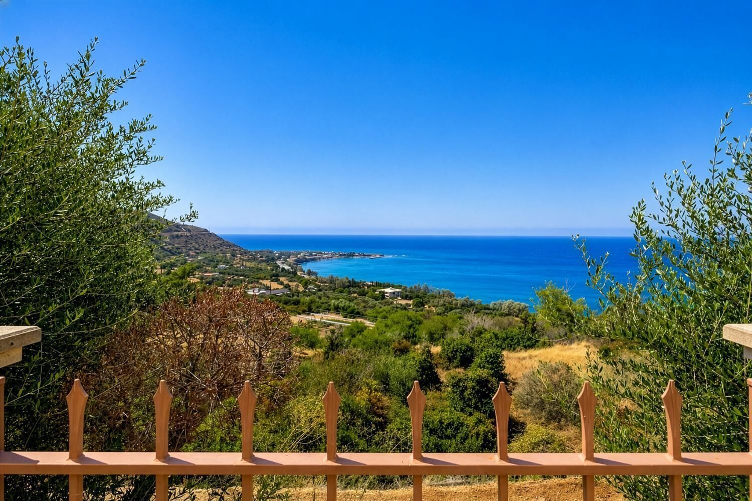 Paisaje costero con vista al mar, una valla de madera y follaje.